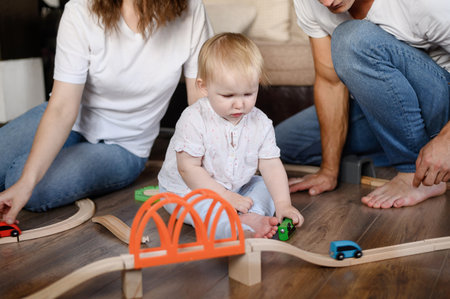 Young parents with their child spend time together, sitting on the floor at home, enjoying games, playing wooden railwayの写真素材