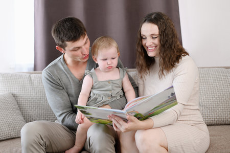 Parents read a book to their child, look at educational pictures, sitting on couch at home.Happy family concept,learningの写真素材