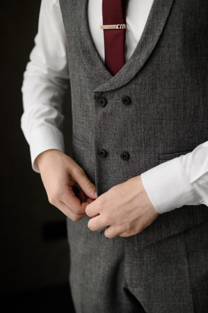 Fashionable business man wearing a tie fastening a button on a gray stylish jacket, close-up. Men fashion concept, wedding day, young modern businessman, men's stylish clothing.の写真素材
