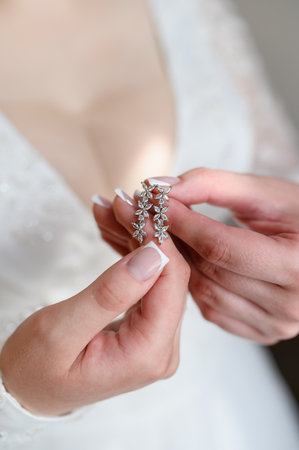 Beautiful earrings in hands of bride, close-up. Concept of bride's morning, preparation for wedding ceremony, wedding day. Stylish wedding accessory for the bride. Verticalの写真素材