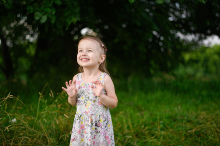 Portrait of a little girl in a dress, smiling, having fun, walking through a meadow in the park....