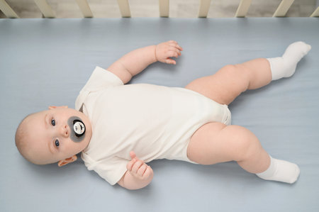 Cute infant lies in crib with pacifier in his mouth. Healthy sleep of newborn baby in wooden crib....