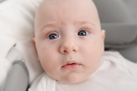Portrait of cute serious baby lying in cocoon of a baby lounger, looking at camera, close-up....