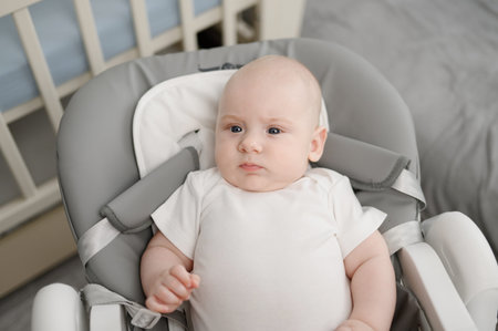 Cute baby is awake on high chair, baby lounger, and spends his time actively. Portrait of newborn...