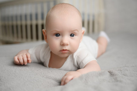 Cute infant lying on stomach in bed, tummy time. Concept of strengthening muscles, preventing infant...