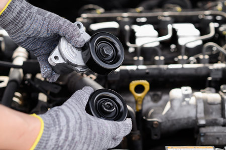 Man in work gloves holds against background of engine compartment of car, bypass and parasitic...