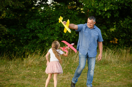 Happy girl and dad having fun outdoors, playing with toy airplane, running with it, in park on grass, smiling happily. Childhood and dream concept, father and child games. International Fathers Dayの写真素材