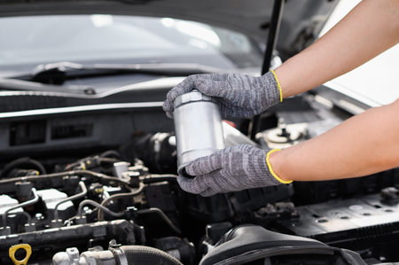 Auto mechanic holding fuel filter for diesel cars against background of car engine compartment. Man working intently under hood of vehicle to ensure it works properly. Car maintenance, repair servicesの写真素材