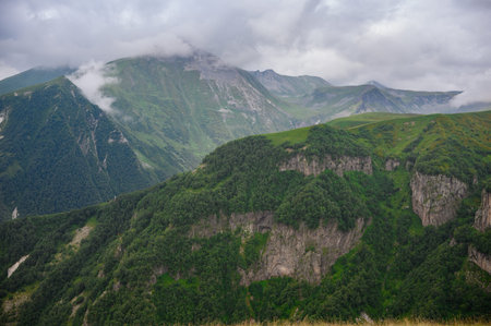 Picturesque view of vast mountain range with lush green trees and white clouds above mountains....