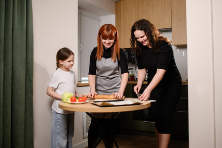 Happy family cooking together in kitchen. Two women and girl have fun cooking. Happy parents enjoy weekend with little girl, making pies at home, pizza. Parental relationship, cooking at homeの写真素材