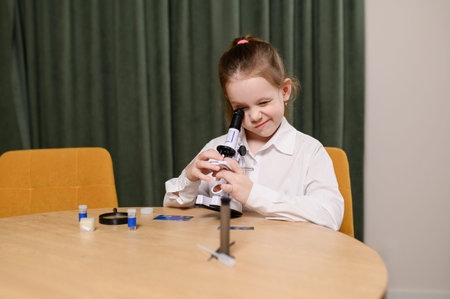 Curious girl looks through microscope while sitting at homeschool table, completing assignments and...