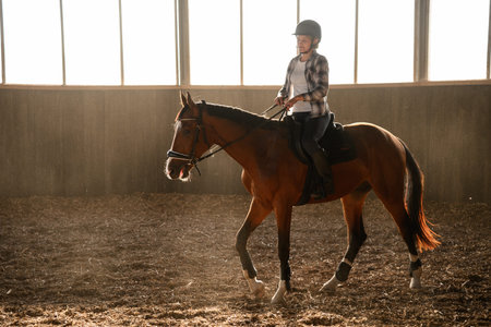 Riding practice in indoor arena. Female rider practicing dressage in sunlit arena, teaching horse to...