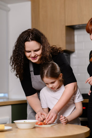 Mother and daughter bond by cooking together in kitchen. Woman helps girl chop vegetables and teaches how to make salad. Cooking together as family. Teaching daughter culinary skills, hobbies.の写真素材