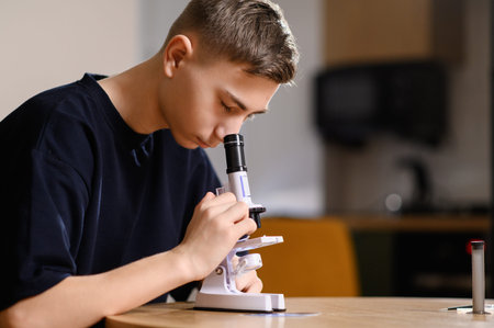 Teenager sits at table, intently examining microscope slide, carefully focusing and adjusting lens....