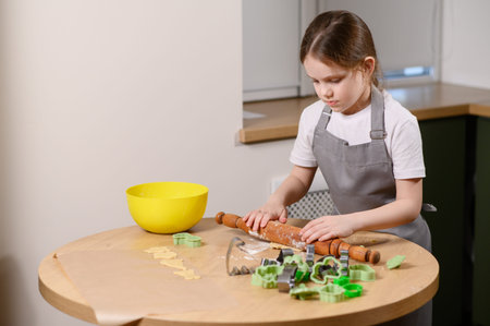 Girl rolls out dough with wooden rolling pin in modern kitchen, cutting out cookie cutters and...