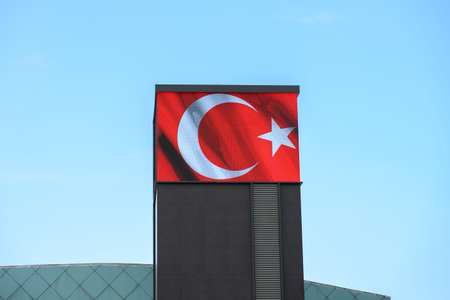 Large Turkish flag on digital display against sky. Modern sports arena features prominent Turkish...