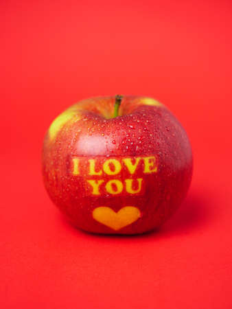 Valentine's Day themed apple with I Love You message and a heart symbol on a red backgroudの写真素材