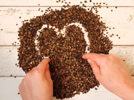 Female drawing a heart symbol in the pile of organic buckwheat husks on a wooden planks background, used as a filling for buckwheat pillowの写真素材