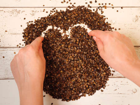 Female drawing a heart symbol in the pile of organic buckwheat husks on a wooden planks background, used as a filling for buckwheat pillowの写真素材