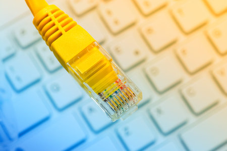 Macro of a yellow network cable in front of a computer keyboard