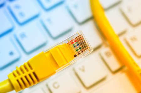 Macro of a yellow network cable in front of a computer keyboardの写真素材