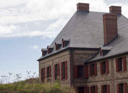 A stone building with red shutters against a blue and white summer sky located at Fortress Louisbourg, Cape Breton, Nova Scotia, a National historic site.のeditorial素材