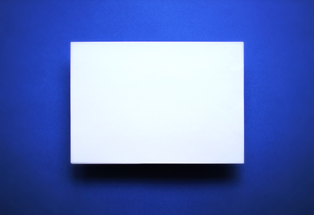 Empty white paper sheet isolated on blue backgroundの写真素材