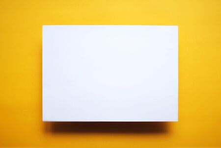 Empty white paper sheet isolated on yellow backgroundの写真素材
