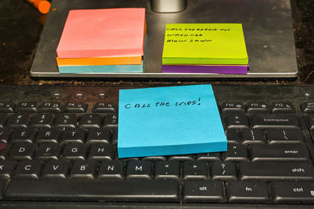 Computer keyboard with a note stating "call the kids" and other colorful note pads including one with a todo list.の写真素材