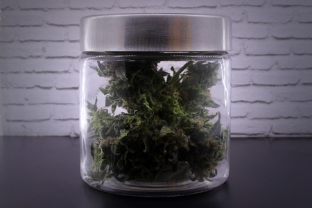 Fragrant marijuana buds in glass jar on a black table and with a white backgroundの写真素材