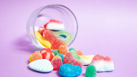 Colorful candies in a glass jar on a purple background.の写真素材