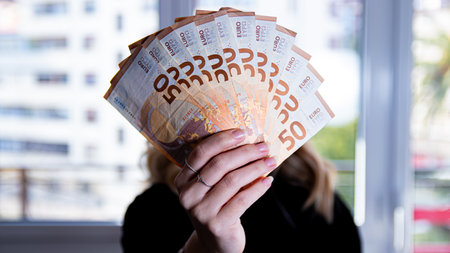 Woman holding euro banknotes in front of her face in a conceptual imageの写真素材