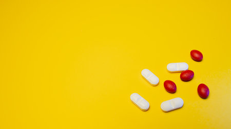 Red and white pills on yellow background. Top view with copy spaceの写真素材