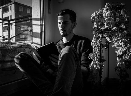 Handsome young man reading a book at home. Black and white photos.の写真素材