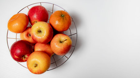 Apples and tangerines in a metal basket on a white background