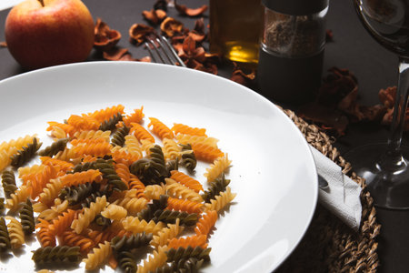 Fusilli pasta on a white plate with red apples and spicesの写真素材