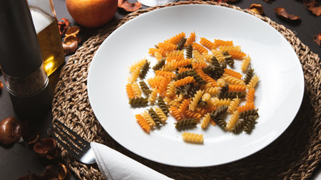 Fusilli pasta on a white plate with a fork and knifeの写真素材