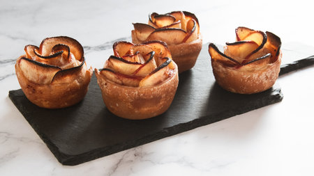 baked apples with rose petals on black slate board over white marble backgroundの写真素材