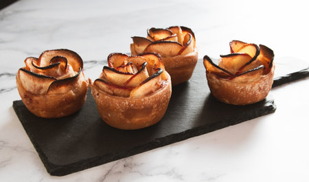 Baked apples with rose petals on black slate plate over white marble backgroundの写真素材