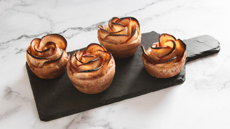 Apple tarts with rose petals on black slate board over white marble backgroundの写真素材