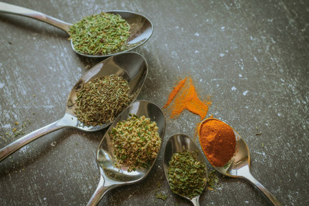 Spices in metal spoons on black stone table. Toned.の写真素材