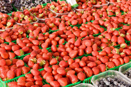 Fresh Strawberrys on display and for sale at farmers market with grapes in foreground and background の写真素材