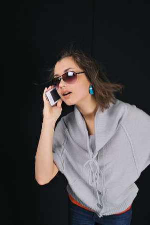 Smiling girl to call by phone close up, on black background.の写真素材