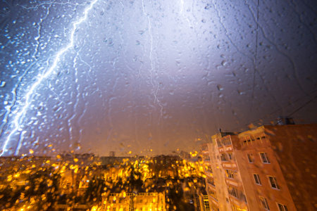 Clouds and thunder lightnings and storm over city. With drops on glass