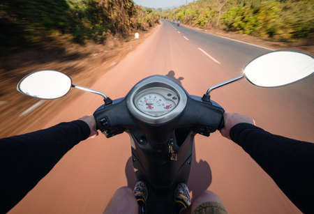 Rider driving scooter on an asphalt road. Motion blurred background. First-person viewの写真素材