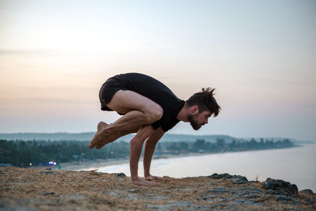 Healthy man practicing yoga under the beach at sunsetの写真素材