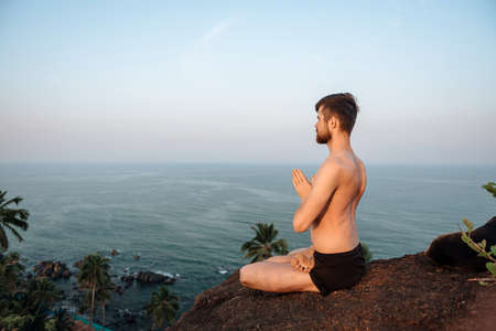 Healthy man practicing yoga under the beach at sunsetの写真素材