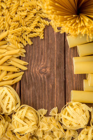 Different kinds of pasta on a wooden background. Farfalle, fettuccine, noodles, fusilli and penne rigate.の写真素材