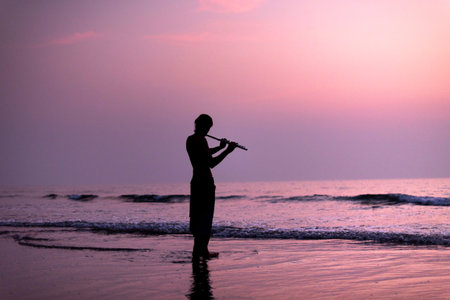 A man is practicing playing the flute on the birch in the sunset. GOA, India. 16.01.2018.