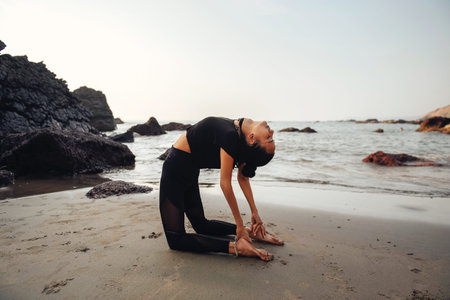 Young healthy woman practicing yoga on the beach at sunset.
